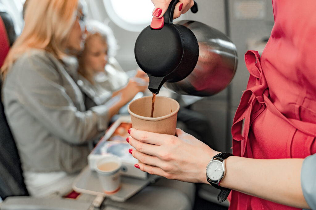 Flight attendant holding teapot and paper cup serving coffee to a mother and child on an airplane