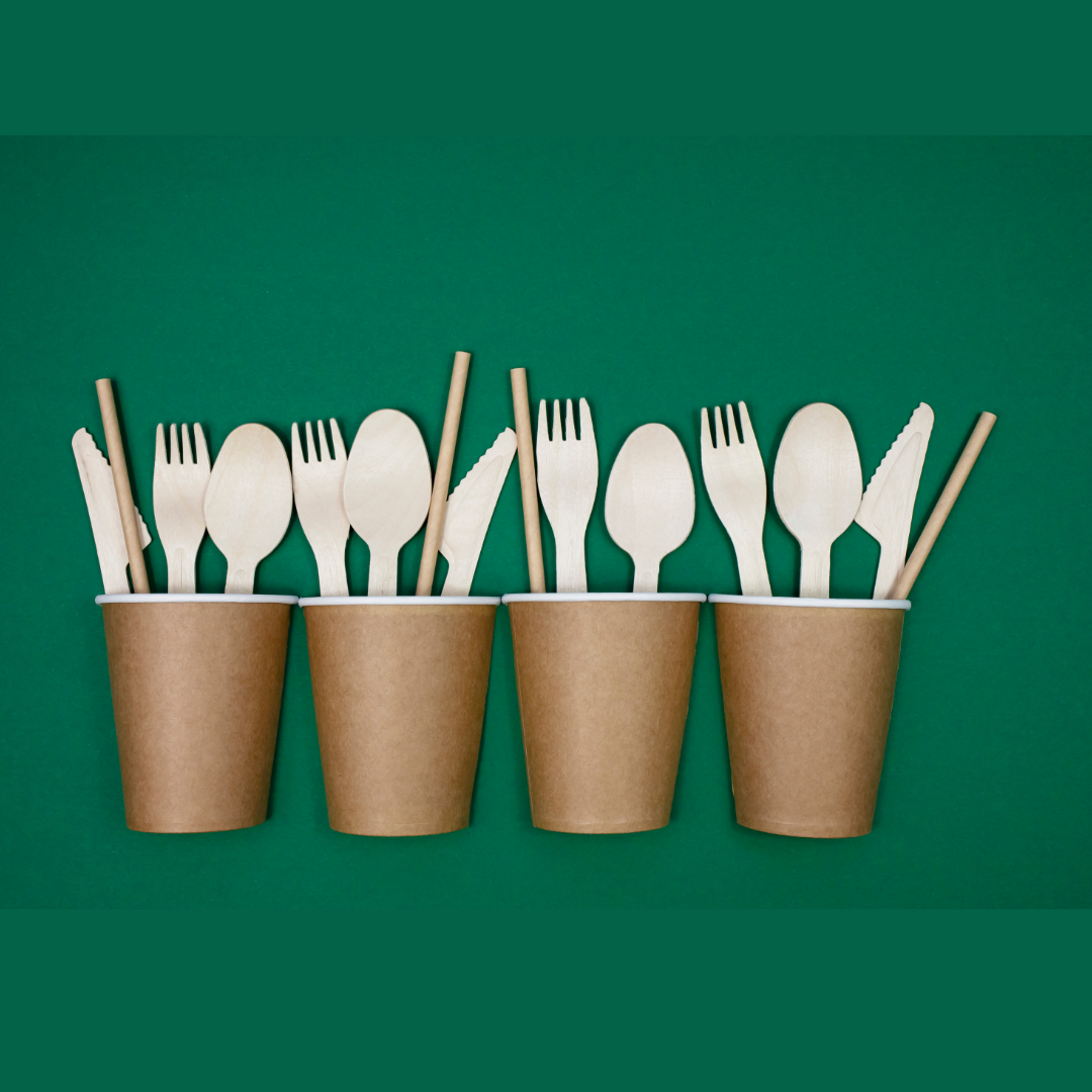 Paper cups and wooden utensils on a green background. Perfect for eco-friendly gatherings.