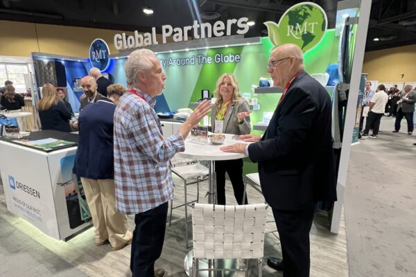 Attendees converse at a trade show booth near a 'Global Partners' sign for RMT, with other exhibitor booths visible in the background.